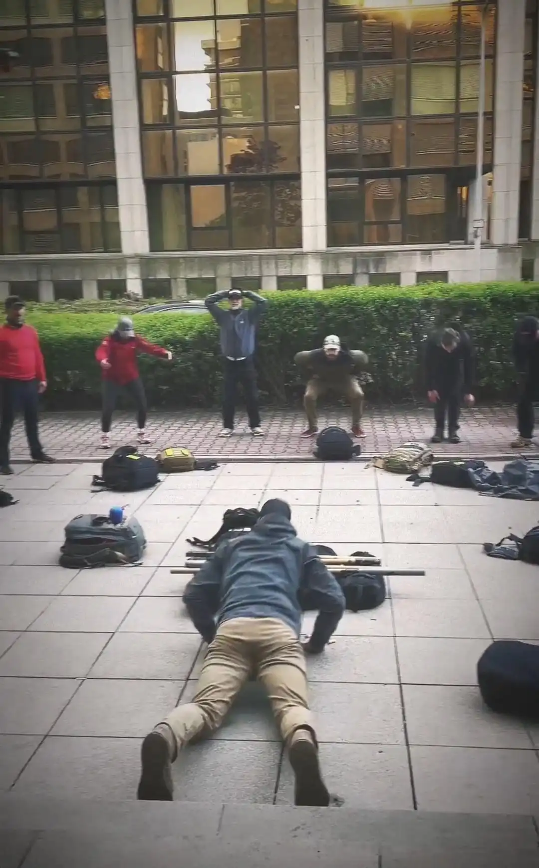Image: View of participants standing in a half-circle, with the leader in the middle. The group is doing burpees.